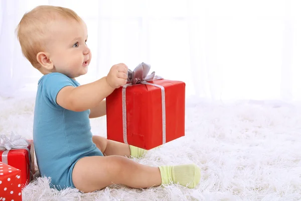 Schattige babyjongen met huidige doos op tapijt in kamer — Stockfoto