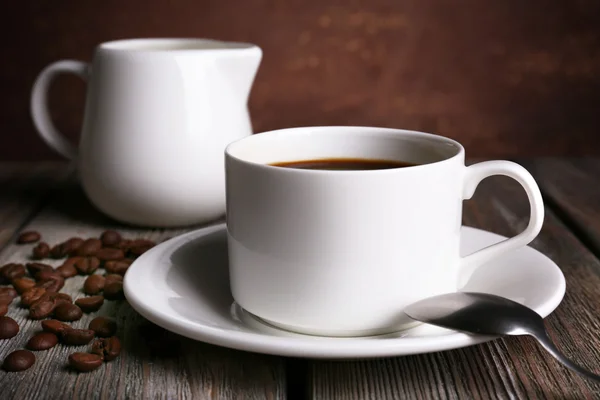 Tazza di caffè con crema in brocca di latte e chicchi di caffè su tavolo di legno su sfondo scuro — Foto Stock