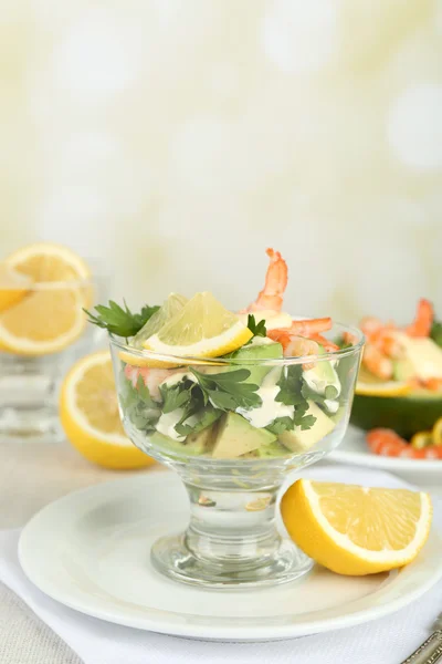 Salades savoureuses avec crevettes et avocat dans un bol en verre et sur l'assiette, sur la table, sur un fond lumineux — Photo