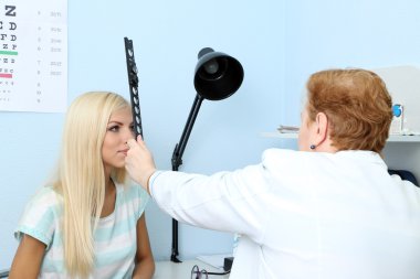 Optometry concept - pretty young woman having her eyes examined by eye doctor  clipart