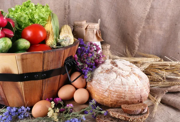 Великий круглий дерев'яний кошик з овочами, молоком і хлібом на мішковому тлі — стокове фото