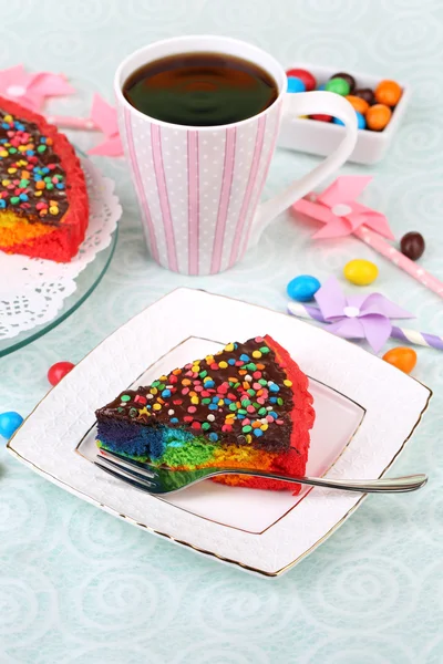 Delicioso pastel de arco iris en el plato y la taza con café, en la mesa, sobre fondo claro — Foto de Stock