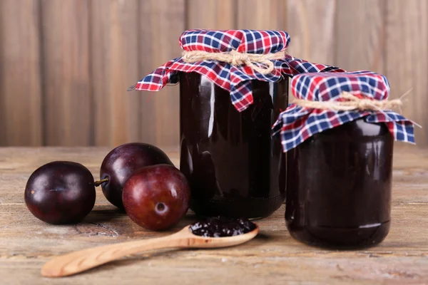 Confiture de prunes savoureuse dans des pots et des prunes sur une table en bois — Photo