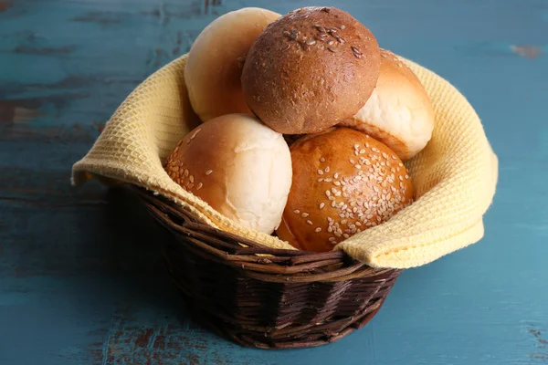 Petits pains savoureux au sésame dans un panier en osier, sur fond de bois couleur — Photo