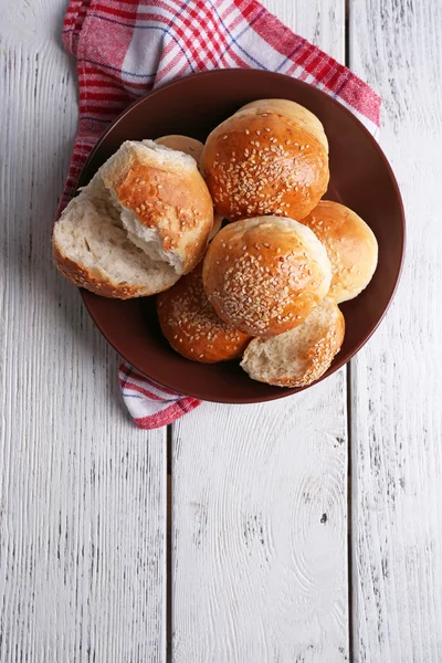 Tasty buns with sesame on plate, on color wooden background — Stock Photo, Image