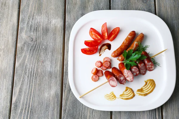 Assortment of tasty thin sausages on plate, on wooden background — Stock Photo, Image