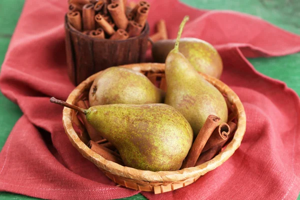 Pere mature e bastoncini di cannella in cesto di vimini, su sfondo di legno a colori — Foto Stock