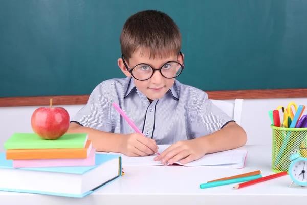 Skolpojke sitter i klassrummet på blackboard bakgrund — Stockfoto