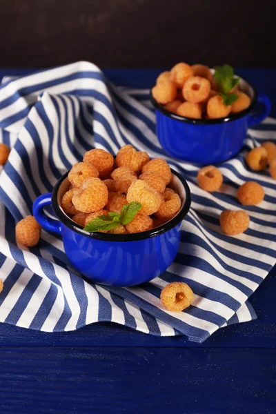 Yellow raspberries in dark blue mugs on napkin on table on dark background — Stock Photo, Image