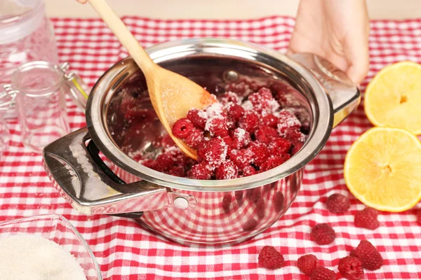 Красная малина в металлической сковороде, сахар, лимон и стеклянные банки на фоне ткани — стоковое фото