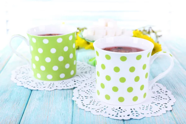 Deux tasses à pois de thé avec du sucre et des fleurs sauvages sur des serviettes sur une table en bois sur fond clair — Photo