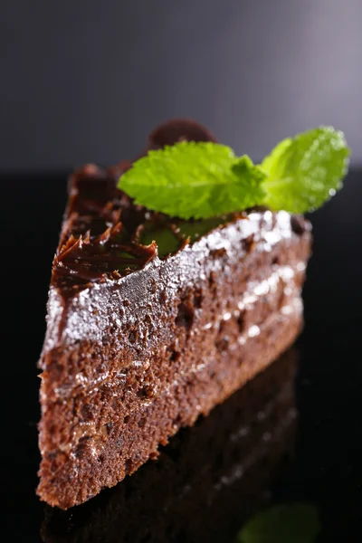 Piece of chocolate cake with mint leaves on glass table on dark background — Stock Photo, Image
