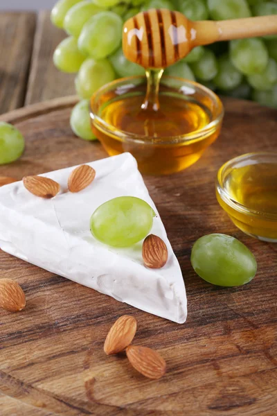 Brie, miel dans un bol en verre, noix et raisins sur fond de bois — Photo