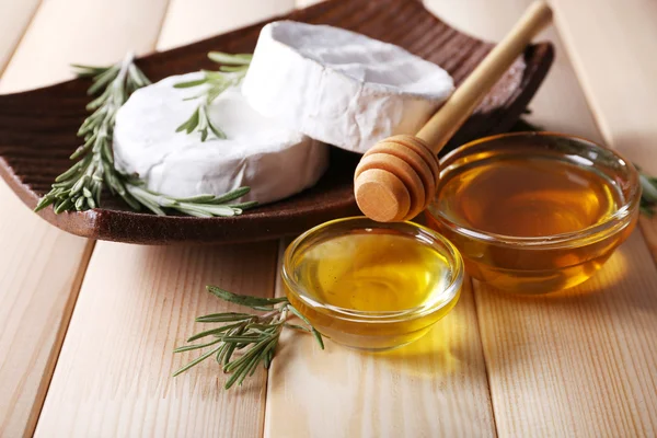 Camembert cheese on plate, honey in glass bowls on wooden background — Stock Photo, Image