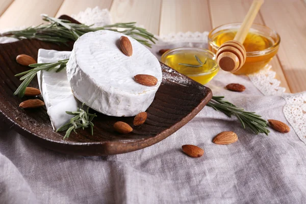 Brie and Camembert cheese with nuts on plate, honey in glass bowl on napkin on wooden background — Stock Photo, Image