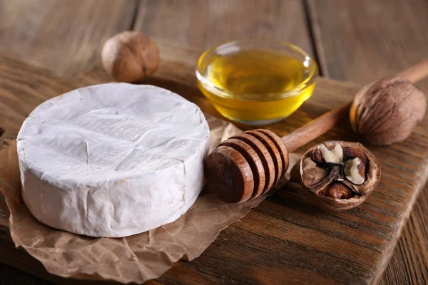 Camembert kaas op papier, honing in glazen kom en noten op snijplank op houten achtergrond — Stockfoto