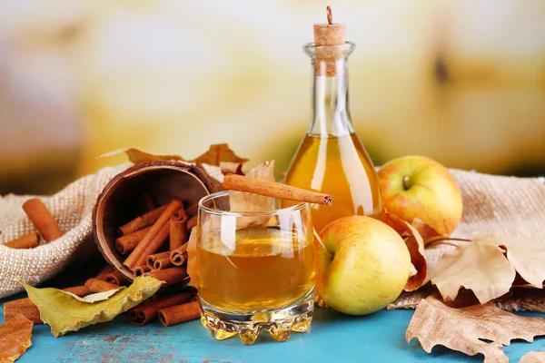 Composition du cidre de pomme avec bâtonnets de cannelle, pommes fraîches et feuilles d'automne sur table en bois, sur fond lumineux — Photo