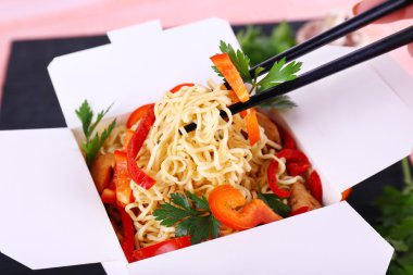 Çin eriştesi ve paket servisi olan restoran kutusunda pembe bir arka plan üzerinde siyah mat sopa