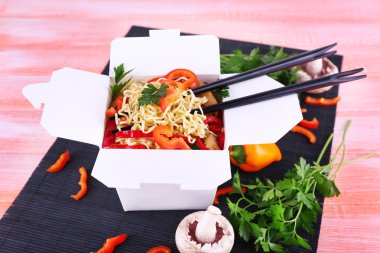 Çin eriştesi ve paket servisi olan restoran kutusunda pembe bir arka plan üzerinde siyah mat sopa
