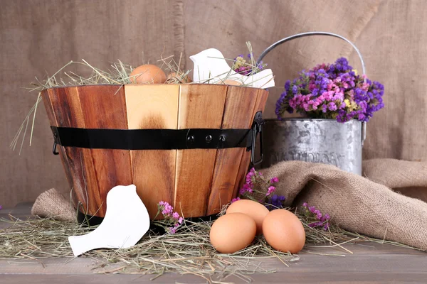 Big round basket with dried grass and fresh eggs on sacking background — Stock Photo, Image
