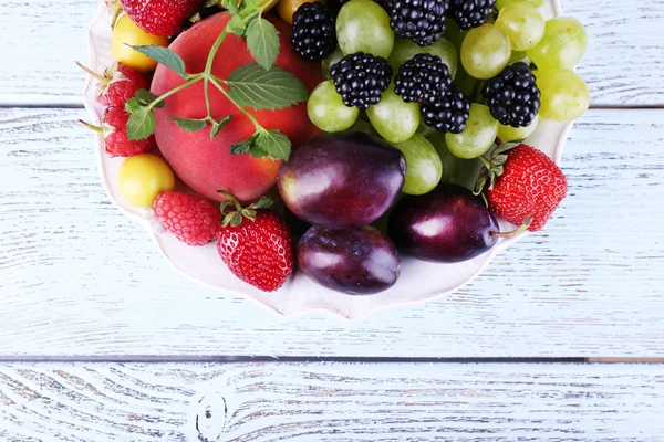 Different berries and fruits in plate on wooden table close-up — Stock Photo, Image