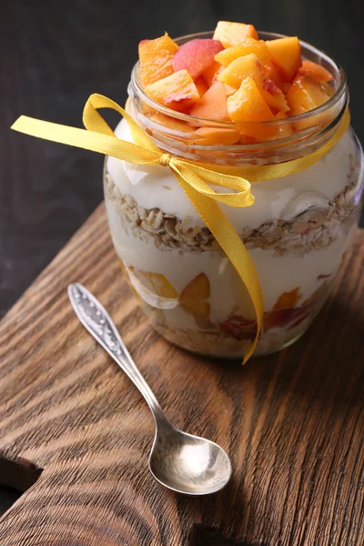 Desayuno saludable yogur con melocotón fresco y muesli servido en frasco de vidrio, sobre fondo de madera —  Fotos de Stock