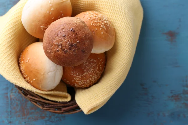 Tasty buns with sesame in wicker basket, on color wooden background — Stock Photo, Image