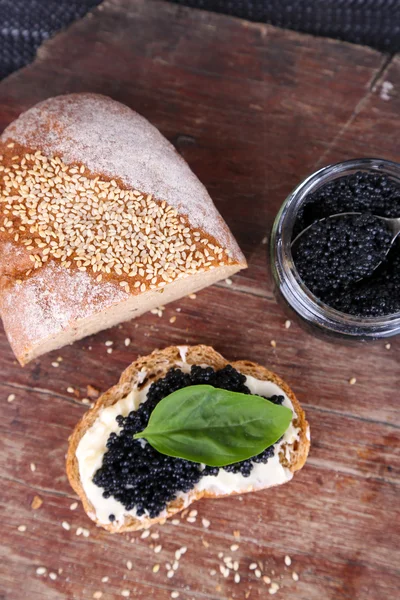 Slices of bread with butter and black caviar on wooden background — Stock Photo, Image