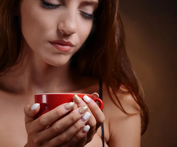Mooi meisje met kop koffie op bruine achtergrond — Stockfoto