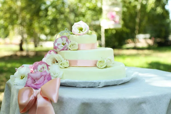 Bolo de casamento bonito com flores na mesa, ao ar livre — Fotografia de Stock