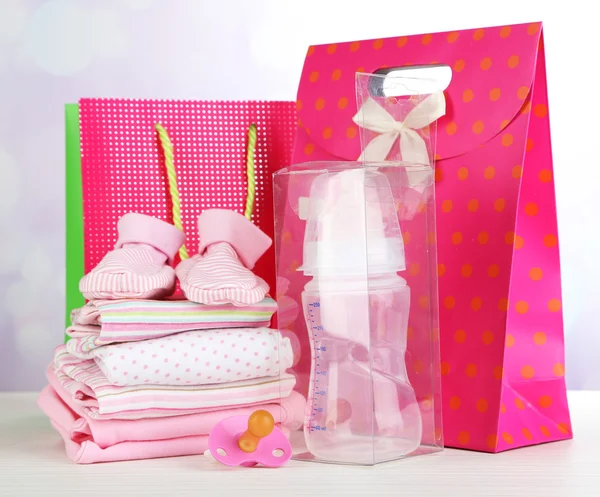 Roupas de bebê e sacos de presente no fundo brilhante — Fotografia de Stock
