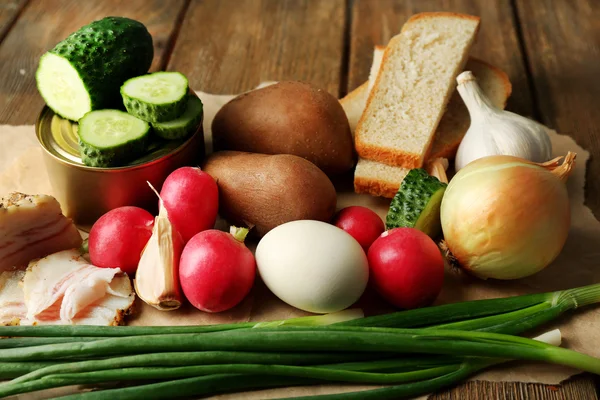 Spek, verse groenten, gekookt ei en brood op papier, op houten ondergrond. Ontbijtconcept dorp. — Stockfoto
