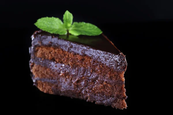 Stuk van chocolade taart met munt laat op glazen tafel op donkere achtergrond — Stockfoto