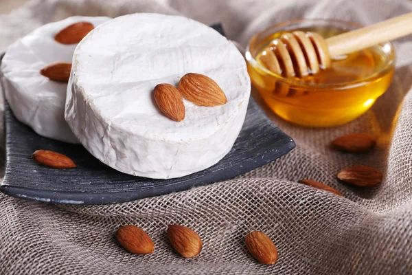 Queijo camembert em prato, mel em tigela de vidro e nozes em fundo de pano de saco — Fotografia de Stock