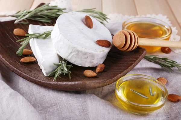 Brie and Camembert cheese with nuts on plate, honey in glass bowl on napkin on wooden background — Stock Photo, Image