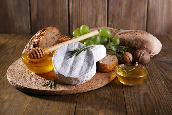 Camembert formaggio, pane, miele e uva sul tagliere su sfondo di legno — Foto Stock
