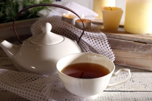 Sammansättning med te i koppen och tekanna och ljusen på bordet, på ljus bakgrund — Stockfoto