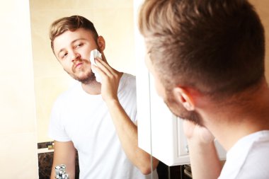 Genç adam banyoda sakalını kesiyor.