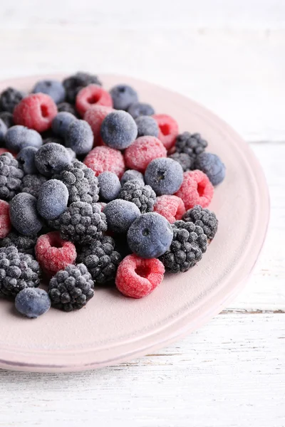 Iced berries on plate, on color wooden background — Stock Photo, Image