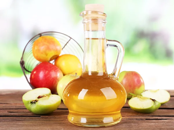 Apfelessig in Glasflasche und reifen frischen Äpfeln, auf Holztisch, auf Naturhintergrund — Stockfoto