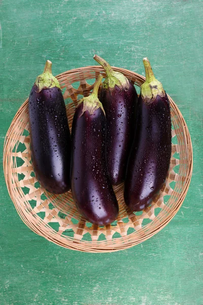 Aubergines in wicker basket on wooden background — Stock Photo, Image