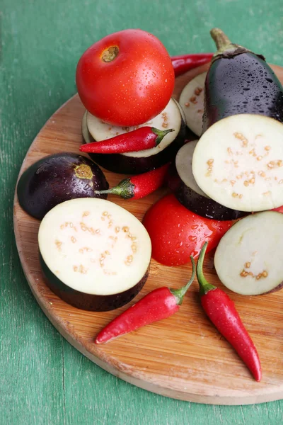 Chopped aubergines with tomatoes and chilly pepper on cutting board on wooden background — Stock Photo, Image