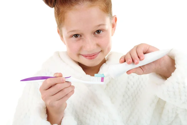 Hermosa niña en albornoz sosteniendo cepillo de dientes y pasta de dientes aislados en blanco —  Fotos de Stock