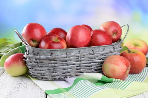 Manzanas dulces en canasta de mimbre sobre mesa sobre fondo brillante — Foto de Stock