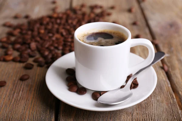 Xícara de café e grãos de café em guardanapo em fundo de madeira — Fotografia de Stock