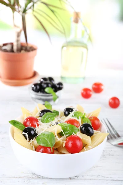 Pasta met tomaten, olijven en basilicum bladeren in kom op servet op houten tafel op natuurlijke achtergrond — Stockfoto