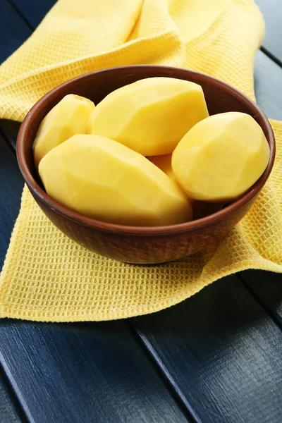 Patatas peladas crudas en tazón sobre fondo de madera de color —  Fotos de Stock