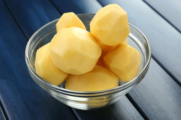 Batatas descascadas cruas em tigela de vidro sobre fundo de madeira cor — Fotografia de Stock