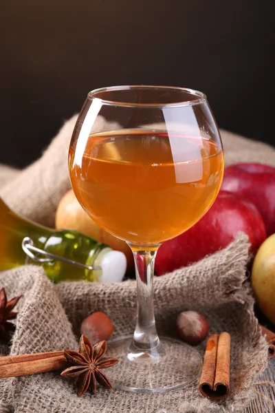 Apple cider in glas wijn en een fles, met kaneelstokjes en verse appelen op tafel, op donkere achtergrond — Stockfoto