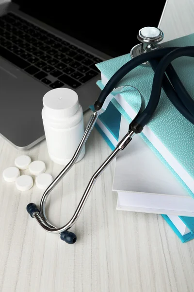 Medical stethoscope with books and laptop on wooden table — Stock Photo, Image